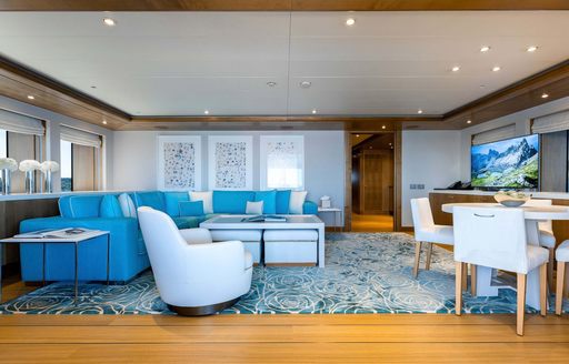 Lounge area onboard charter yacht AIFER, white and teal furnishings dominate with low coffee table and a dining table to starboard.