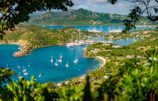 Elevated view looking down on the coastline of Antigua, with many motor yachts and sailing boats at anchor