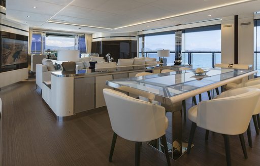 Interior dining area onboard boat charter SANCTUARY with a long glass table surrounded by white seats