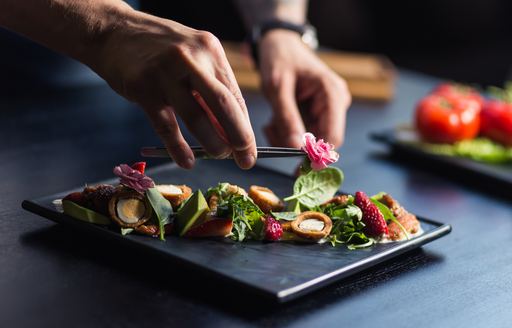 Yacht chef garnishes plate of food with flower 