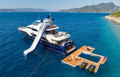 Benetti yacht charter AMADEA in a bay with a slide and host of water toys on the sea.
