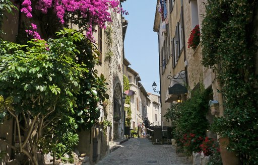 Sunny cobbled streets in town in the French Riviera, with ivy on walls and purple flowers