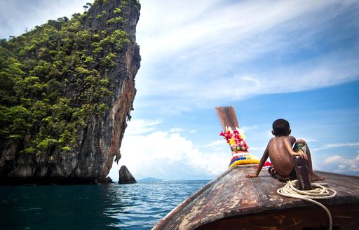 Boy on traditional Thai long-tail boat navigating the waters of Ko Phi Phi on the way to Maya Bay, Thailand.