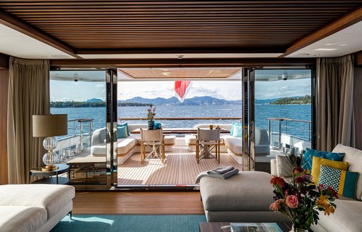 View of the aft deck from the interiors of charter yacht MANA I, alfresco seating visible through open sliding doors and views of the sea in the background