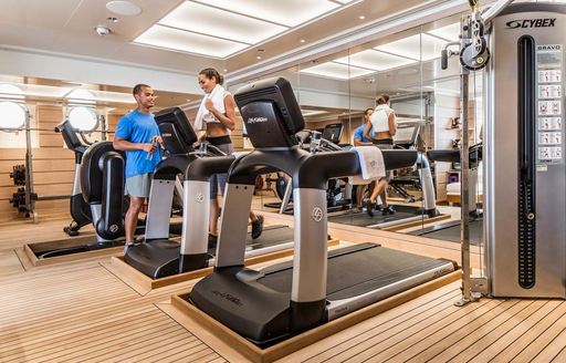 Overview of the gym onboard charter yacht AQUILA, with a charter guest and a trainer