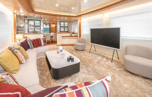 Main salon lounge area onboard charter yacht GELLY, U-shaped white seating with multi-colored cushions and a TV opposite