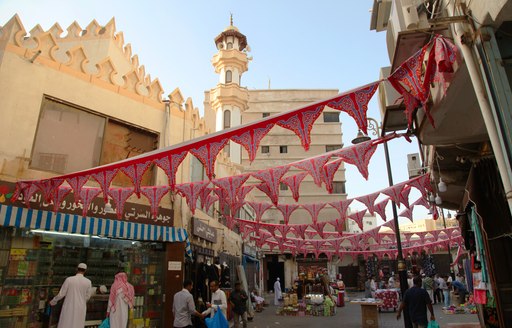 Overview of a street filled with shops during Ramadan. Bunting hung across the street with many visitors walking through.