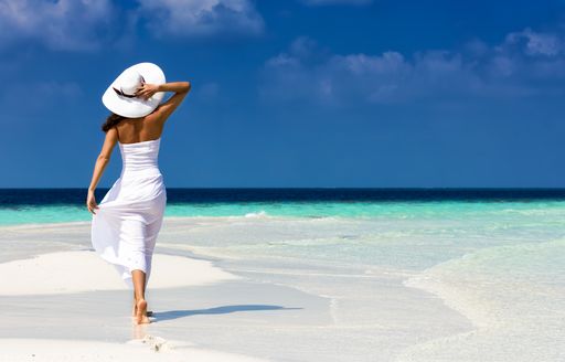 Female charter guest walking on a beach holding her hat 