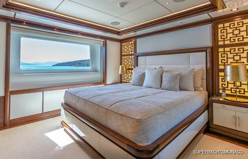 Overview of a guest cabin onboard M/Y IMMERSIVE, central berth facing forward with a wide window looking out over the sea and distant land.