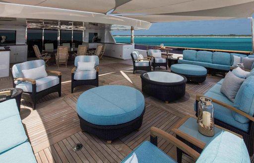 Aft deck onboard charter yacht UNBRIDLED, lounge area with multiple armchairs and three coffee tables, plus sunpads to the side. 