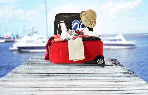 Open red suitcase with vacation apparel on a dock in front of some yachts blurred in the background