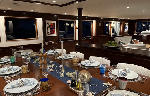 Interior dining area onboard charter yacht GENESIA, long table set for a meal, surrounded by windows
