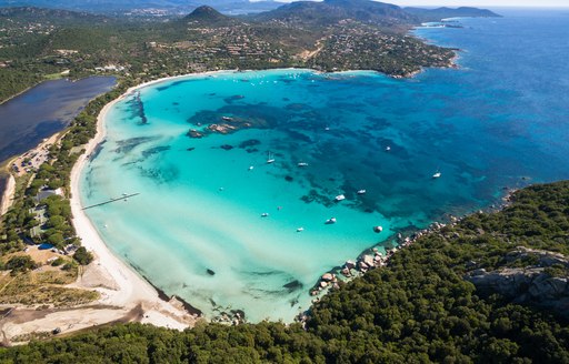 Bright blue water in secluded bay in Sardinia, with Mediterranean terrain surrounding