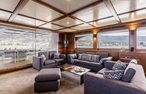 Interior lounge onboard charter yacht KLOBUK, plush gray seating with large windows surrounding