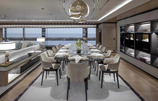 Interior dining area onboard charter yacht MALIA, long dining table with wide reaching windows in the background.