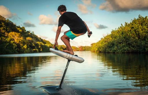 A man rides on an e-foil surfboard in a lake setting
