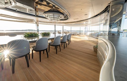 Exterior dining area with a long table and multiple gray seats onboard superyacht charter KISMET