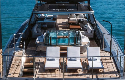 Overview of the aft deck onboard charter yacht ENTERPRISE, with three sunloungers in the foreground and a deck Jacuzzi aft
