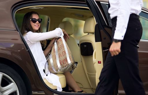 a rich woman in a private car arriving at her destination with prada bag and sunglasses