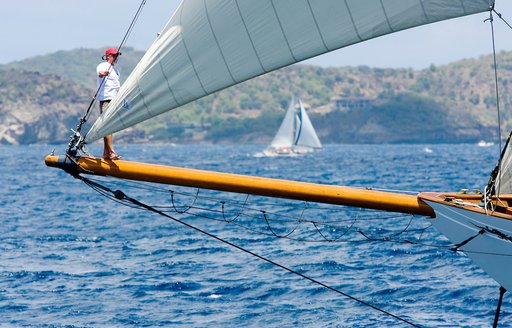 A crew member stands on a classic sail yacht's bow sprite at the Antigua Classic Sailing Regatta