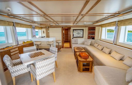 Interiors onboard charter yacht ARTEMISEA, plush cream seating to starboard and a games table to port