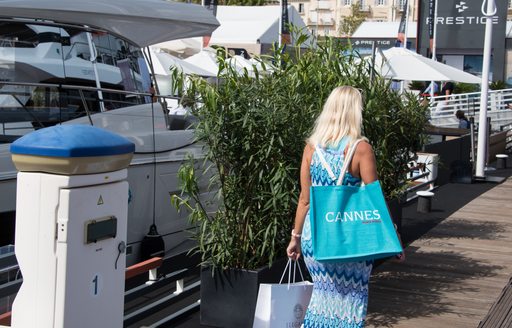 Lady walking along the docks of the Cannes Yachting Festival with shopping bags