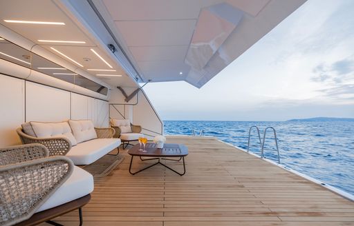 Overview of the swim platform onboard charter yacht OPTIMISM, with white wicker furniture and a low coffee table