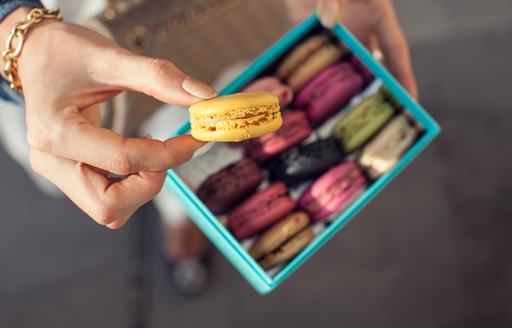 Woman holds yellow macaron from box
