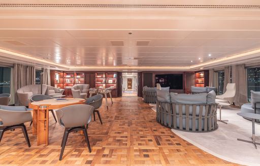 Interiors onboard charter yacht CARINTHIA VII, seating arrangements with tables to port and a white carpet and windows to starboard 