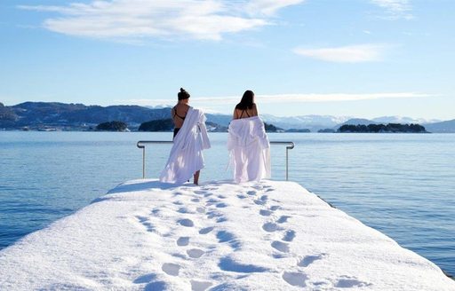 Sea bathers with white dressing gowns contemplate the freezing water off a pontoon thick with snow in Norway 