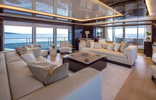 Main salon onboard charter yacht AQUA LIBRA, plush white seating surrounded by full-height windows