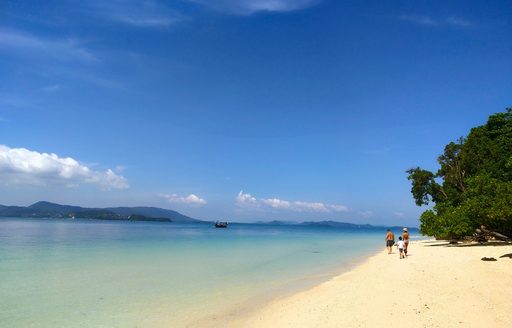 White sand beach in Thailand, clear blue sea and people walking along the shore