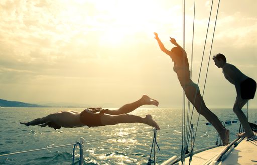 Young people silhouetted against a setting sun as they jump off a yacht