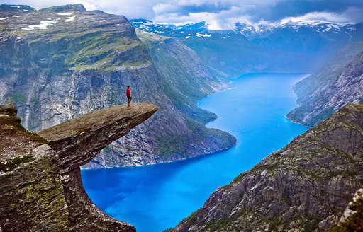 Hiker stands on the edge of Hiker on Trolltunga Rock looking out across the Norwegian Fjords