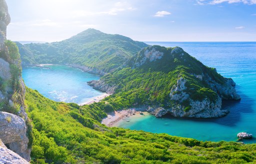 View of the cliff into the crystal clear azure sea bay and distant islands. Unique secluded beach on the Agios Stefanos cape, Corfu in Greece