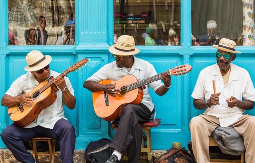 A group of Caribbean locals play music in the street in front of a turquoise shopfront