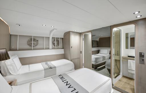 Guest cabin onboard charter yacht ATLANTIKA, with twin berths facing full length mirror and a doorway leading to an en-suite.
