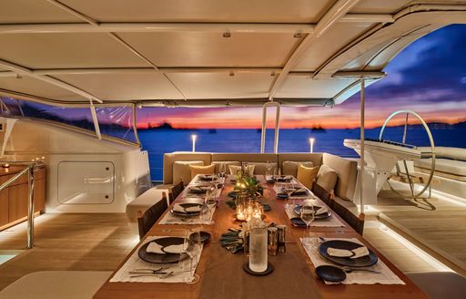 Exterior dining area onboard charter yacht GUILLEMOT, long table surrounded by seating and view of the sea at sunset