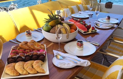 A wooden table is laid with breakfast paraphernalia on the aft deck of a yacht