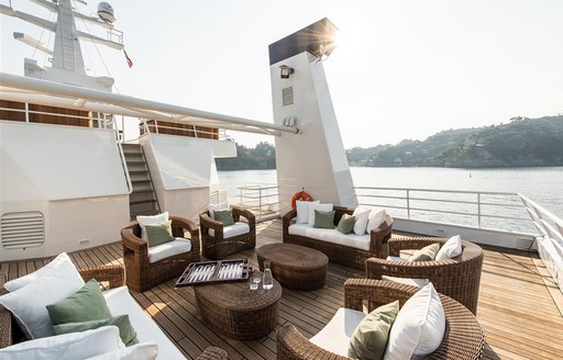 Tables and chairs on sundeck of superyacht 'Bleu De Nimes' with coast in background