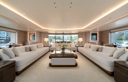 Open plan living room on superyacht O'PARI, with lightly colored sofas and table in center of room with windows all around