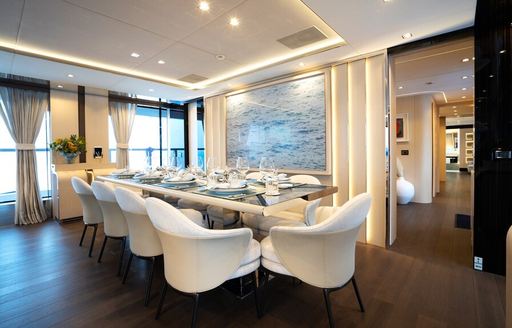 Interior dining area in the main salon onboard private yacht charter HALARA, long dining table with white chairs surrounding