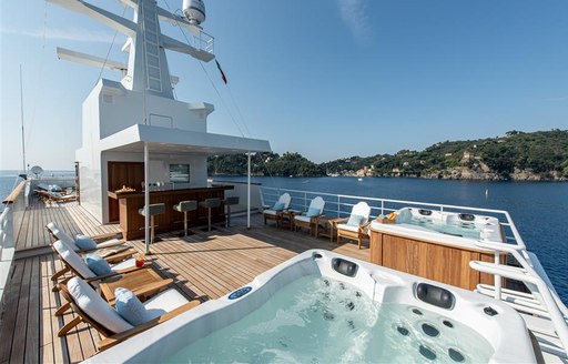 Sundeck on superyacht 'Bleu De Nimes' with double Jacuzzi, sunloungers and coast in background