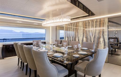 Formal interior dining set up onboard charter yacht PARILLION, long table surrounded by 10 grey upholstered dining chairs