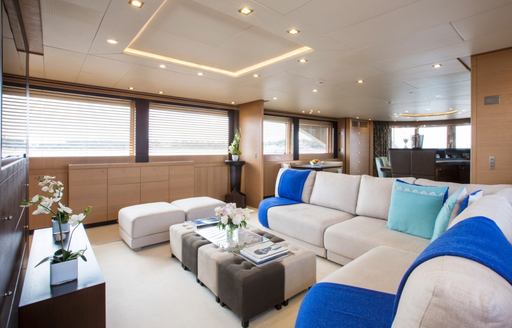 Interior lounge area onboard charter yacht YCM120, corner sofa with blue blankets surrounded by windows