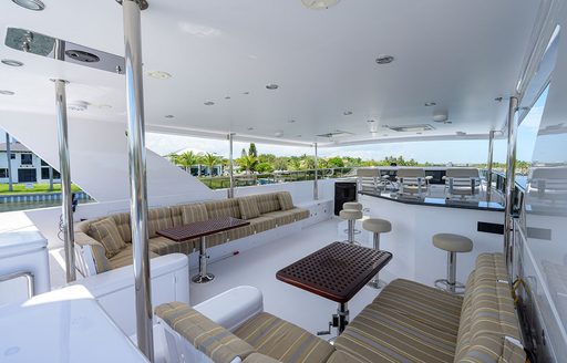 Overview of the flybridge onboard charter yacht NEXT CHAPTER, with alfresco dinette in the foreground and a wet bar with stools aft