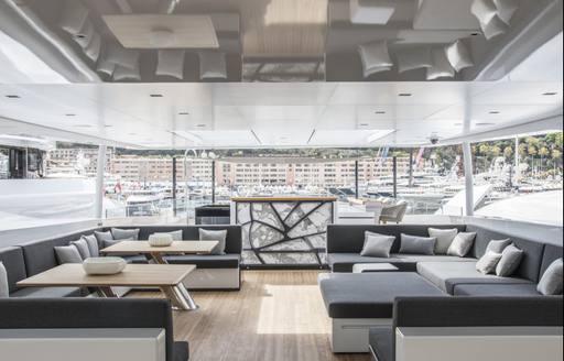 Outdoor covered deck on superyacht SEVERIN'S with wide comfortable seating and yachts and buildings visible in background