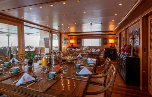 Wooden dining table fully laid out on superyacht 'Bleu De Nimes' with glass sliding doors behind