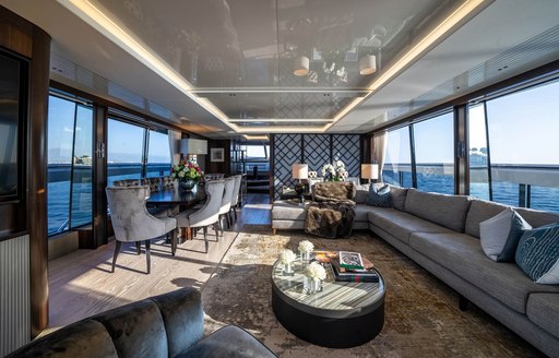 Main salon onboard charter yacht GLASAX, long sofa to starboard and interior dining port, surrounded by large windows