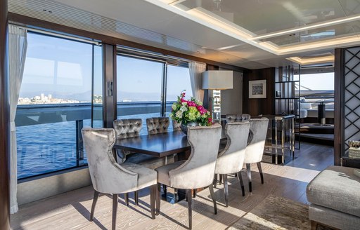 Interior dining setup onboard charter yacht GLASAX, long diing table surrounded by white chairs adjacent to large full-height windows